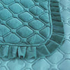 A teal velvet bedspread with a quilted, ruffled edge is shown on a light surface.