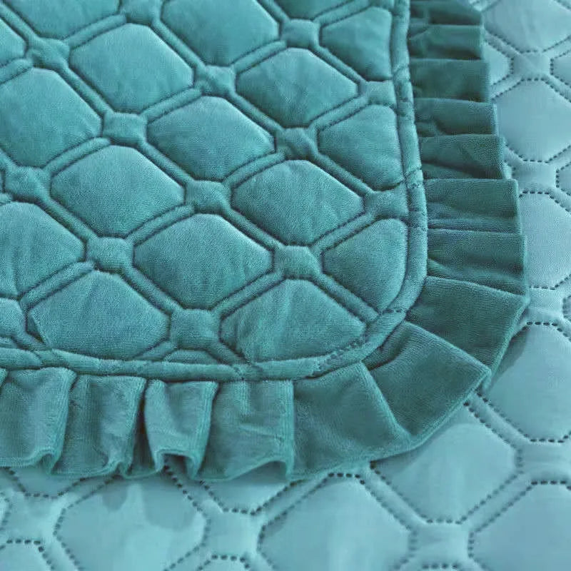 A teal velvet bedspread with a quilted, ruffled edge is shown on a light surface.