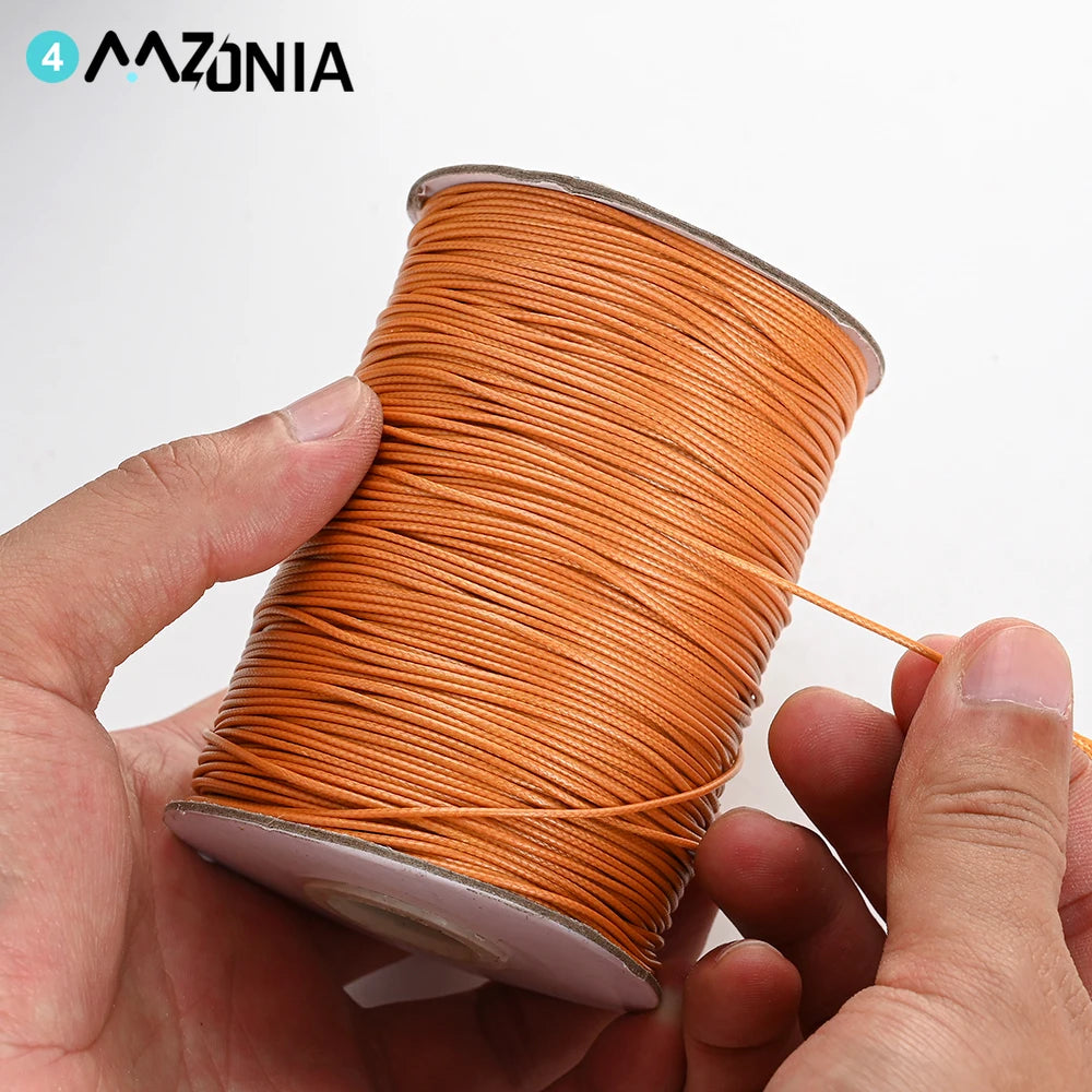 A hand is holding a spool of orange waxed cotton cord for jewelry making.