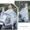 A woman wearing a transparent waterproof motorcycle rain poncho with a hood riding a motorcycle outdoors.