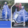 A woman wearing a transparent blue waterproof motorcycle rain poncho with a hood riding a white scooter outdoors.