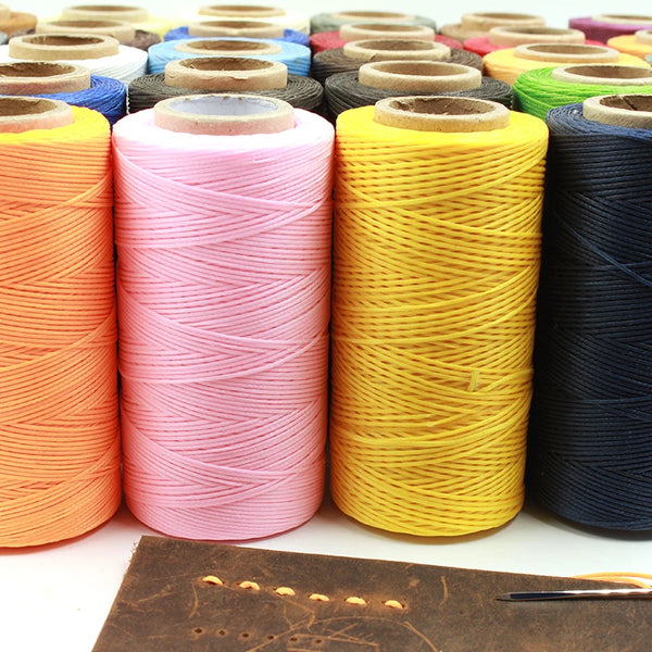 A collection of flat waxed thread spools in various colors, including pink, yellow, and dark blue, resting on a brown leather