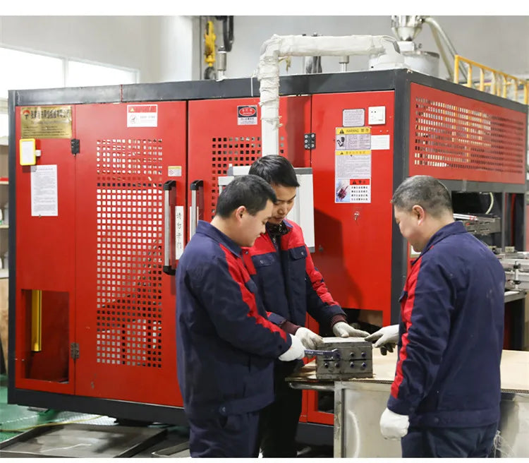 Three workers inspecting a red industrial machine with plastic buckets and lids.
