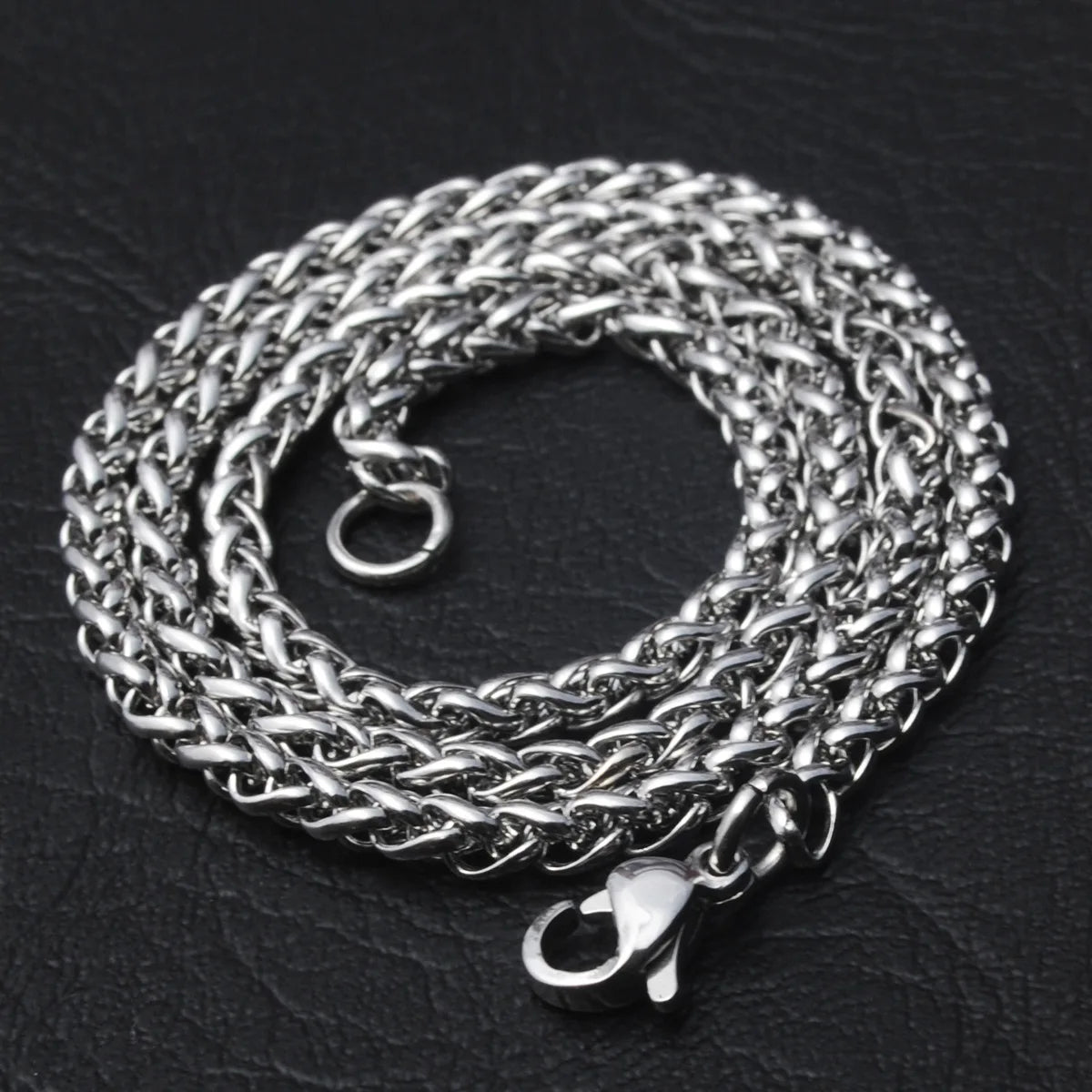 Silver twisted rope chain necklace resting on a black leather surface.