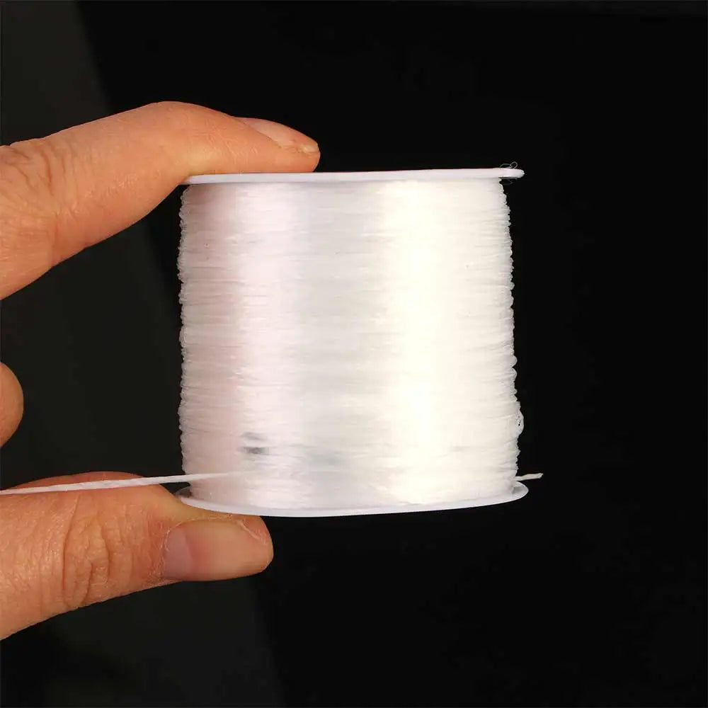 A hand holds a spool of white elastic crystal beading cord for jewelry making.