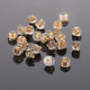 A collection of clear silicone rubber ear back stoppers with copper rings scattered on a dark reflective surface.