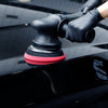 A hand wearing a black glove is using a foam buffing pad on a glossy black car surface.