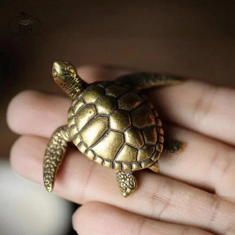 A golden copper turtle figurine is held in a person's hand.
