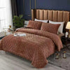 A luxurious brown quilted velvet bedspread with a ruffled edge is displayed on a bed in a bedroom setting.
