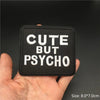 Black embroidered patch with white text that reads CUTE BUT PSYCHO being held in a hand.