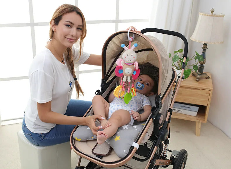 A woman holds a soft plush baby rattle toy with hanging bell and cartoon animal mobile in a stroller for newborns.