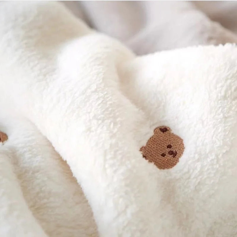 A close-up of a white coral fleece baby blanket with a brown bear embroidery detail.