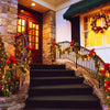 A stone staircase and railing decorated with warm string lights and red flowers leading to a wooden door.