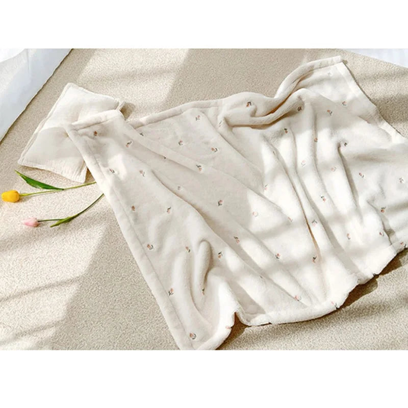 A cream-colored coral fleece baby blanket with subtle bear embroidery draped on a light surface.