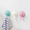 Three suction cup hooks in teal, white, and pink colors mounted on a white surface with a gray striped towel.