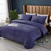 A dark purple quilted velvet bedspread with a textured pattern displayed on a bed.