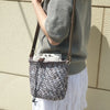 A woman wearing a grey sweater holds an adjustable PU leather crossbody bag with a woven texture.