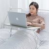 A woman is using an adjustable foldable laptop desk placed on a bed, working on a silver laptop.