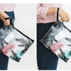 A person is holding a transparent toiletry bag with a hanging hook against a light background.