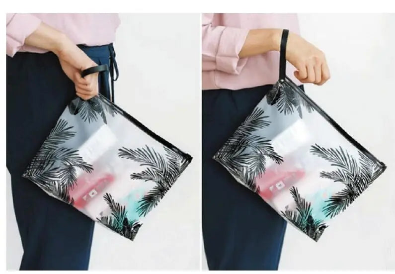 A person is holding a transparent toiletry bag with a hanging hook against a light background.