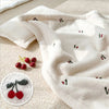A cream-colored coral fleece baby blanket with small red and green bear embroidery is draped on a light background.
