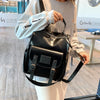 A woman is holding a black PU leather fashion backpack in a light indoor setting.