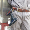 A brown leather tool holster featuring a steel J-hook attached to a belt, worn on light gray pants.