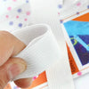 A hand is gripping a white adjustable bed sheet gripper with strong clips, shown next to colorful packaging.