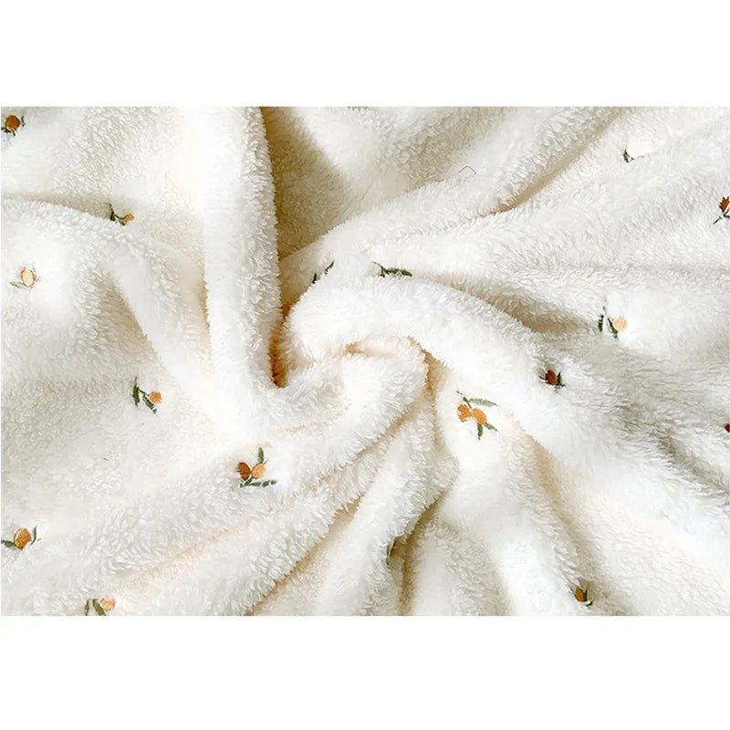 A close-up of a cream colored coral fleece baby blanket with subtle bear embroidery, showing soft texture and folds.
