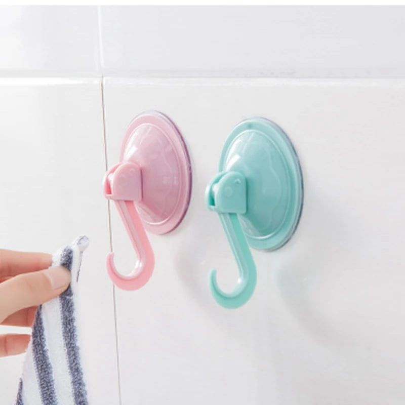 Two suction cup hooks in pink and mint green are mounted on a white surface.