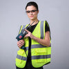 A woman wearing a neon yellow high-visibility safety vest and glasses holds a black tool.