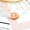 A golden wire fruit brooch pin featuring an orange citrus slice design with white enamel accents.