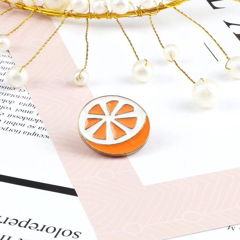 A golden wire fruit brooch pin featuring an orange citrus slice design with white enamel accents.
