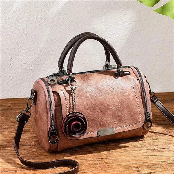 A brown leather crossbody shoulder bag with a floral pendant resting on a wooden surface.