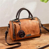 A brown leather crossbody shoulder bag with a floral pendant resting on a wooden surface.