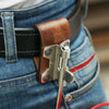 A close-up of a brown leather tool holster hook with a steel J-hook attached to a denim belt.