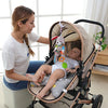 A woman is holding a baby in a stroller featuring a soft plush animal rattle toy and hanging mobile.