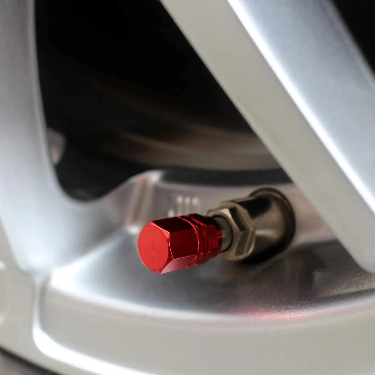 Close-up view of a red aluminum tire valve cap installed on a silver wheel rim.