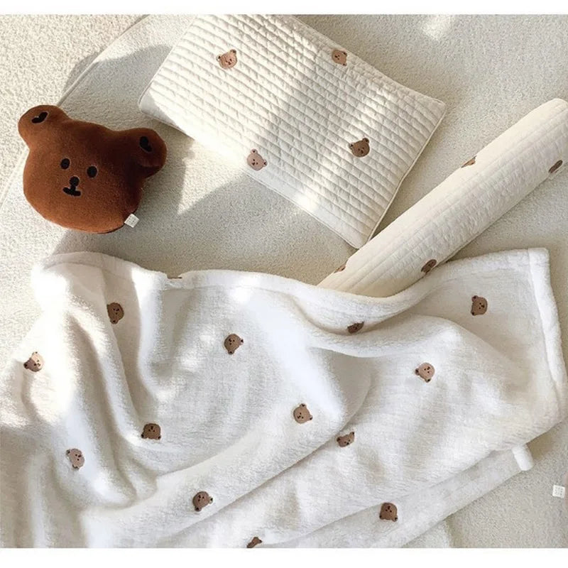 White coral fleece baby blanket with brown bear embroidery shown in various folds and textures.
