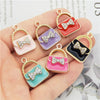 A set of six crystal enamel handbag charm pendants in various colors and designs displayed on a hand.
