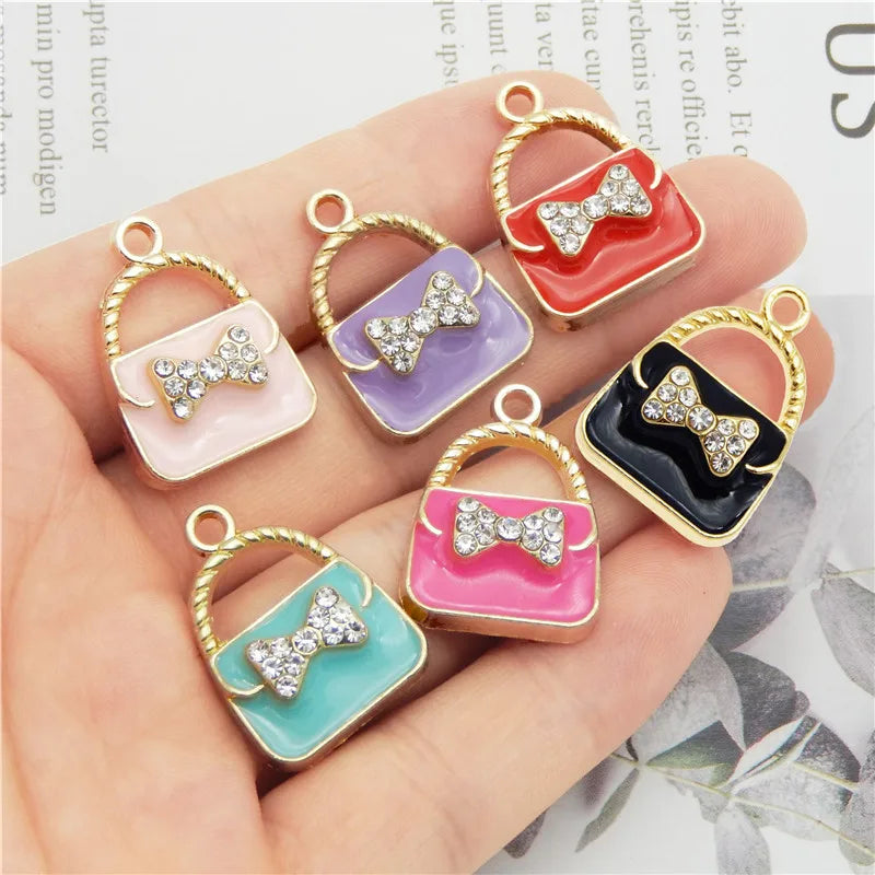 A set of six crystal enamel handbag charm pendants in various colors and designs displayed on a hand.