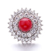 A round, brilliant silver-toned metal snap button with a central red gemstone surrounded by a halo of smaller clear stones.
