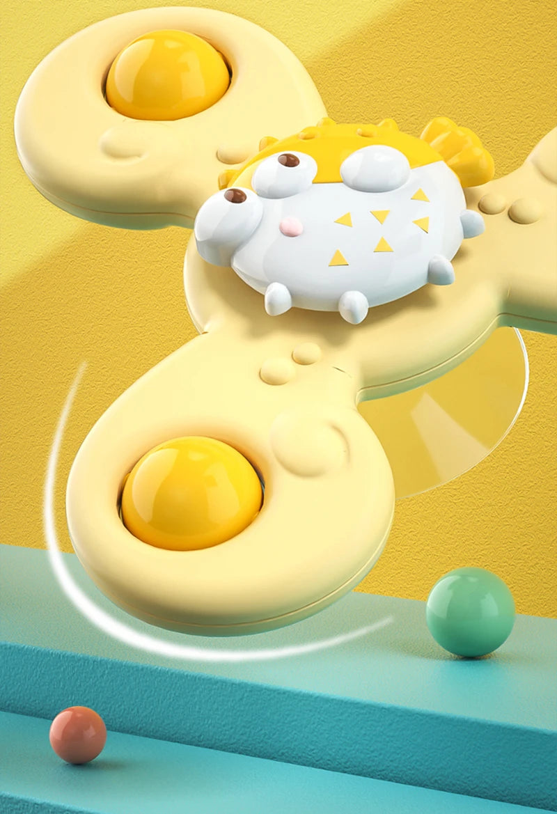 A yellow suction cup spinner bath toy with a white, face-like character and a green ball floating above a blue surface.
