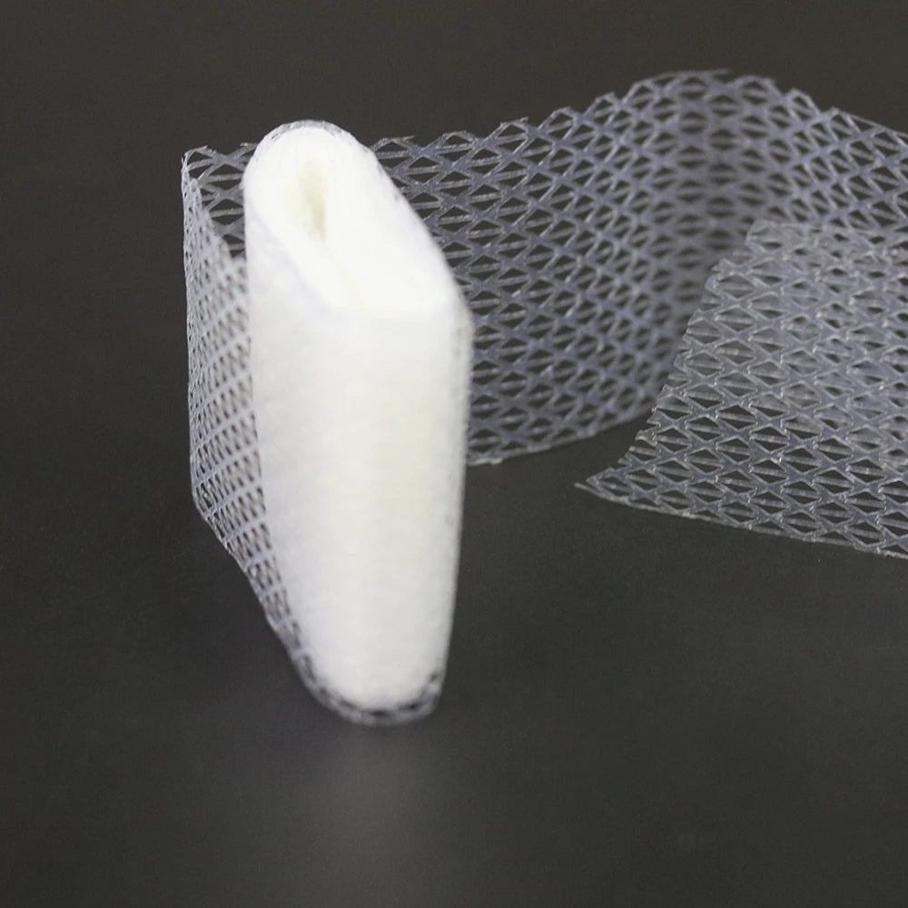Un rouleau de ruban de couture à appliquer sur fer blanc à côté d'un morceau de tissu en maille transparente.