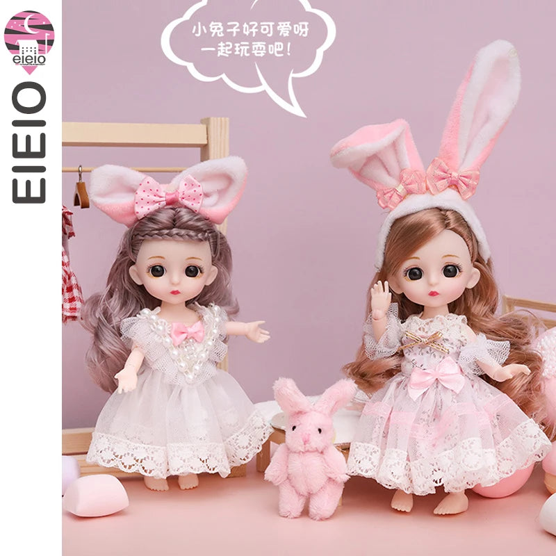 Two pink fashion dolls with large ears and pink dresses stand next to a small pink rabbit.