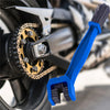 A blue universal chain cleaning brush with bristles is shown next to a motorcycle chain.