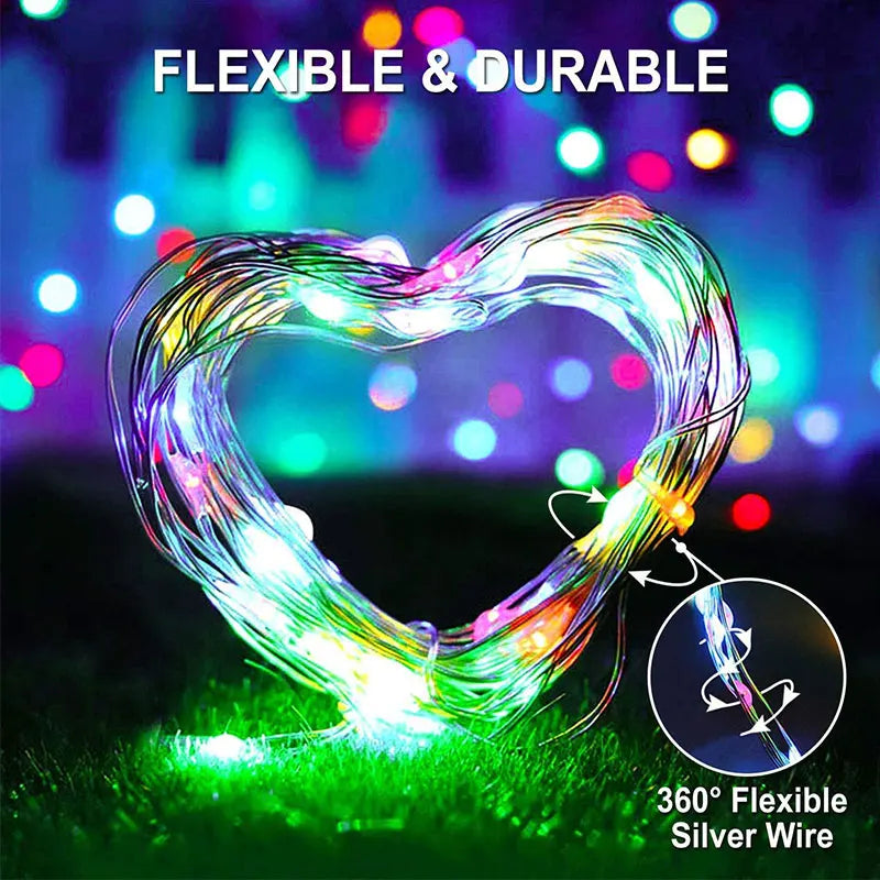 A heart-shaped flexible silver wire light display glowing brightly on green grass.