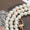A gold-toned pearl chain strap for handbags is displayed on a dark surface.