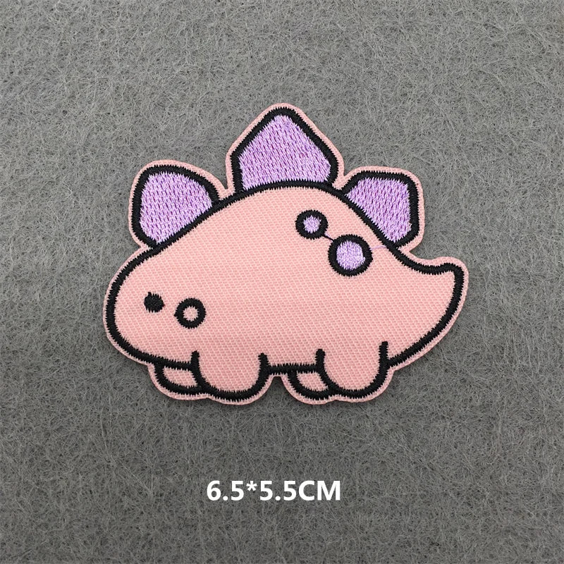 A pink and purple embroidered patch shaped like a stylized dinosaur head on a gray fabric background.