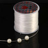 Spool of white stretchy crystal beading cord with pearls unwound on a black surface